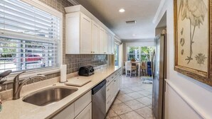 A kitchen with white cabinets, a tiled backsplash, a sink, and a toaster on the counter. - Mermaid’s Purse~Private Pool! 40 steps to beach! (Anna Maria)