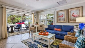 A spacious living area with a blue sofa, wicker chairs, a coffee table, and a dining table. - Mermaid’s Purse~Private Pool! 40 steps to beach! (Anna Maria)