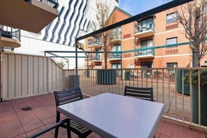 A patio area with a table and chairs, a metal fence, and a building with brick and white walls in the background. - West End City 2BR Stay near UniSA (Adelaide)