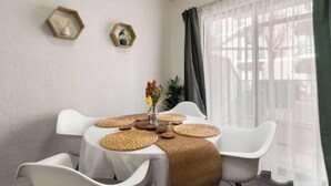 A dining area with a round table, white chairs, woven placemats, and a vase with flowers.