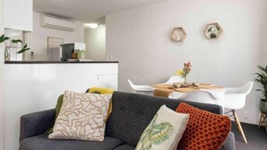 A modern living room with a grey sofa, a dining table with white chairs, and a kitchen in the background.