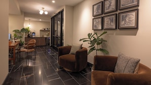 A modern living area with a sofa, armchairs, a dining table, and a kitchen in the background. - The Promissory Hotel (Roanoke)