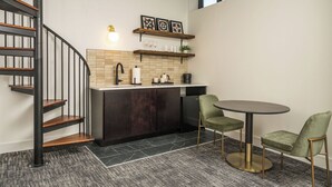 A modern kitchen with a dark wood staircase, a round dining table, and two green chairs. - The Promissory Hotel (Roanoke)
