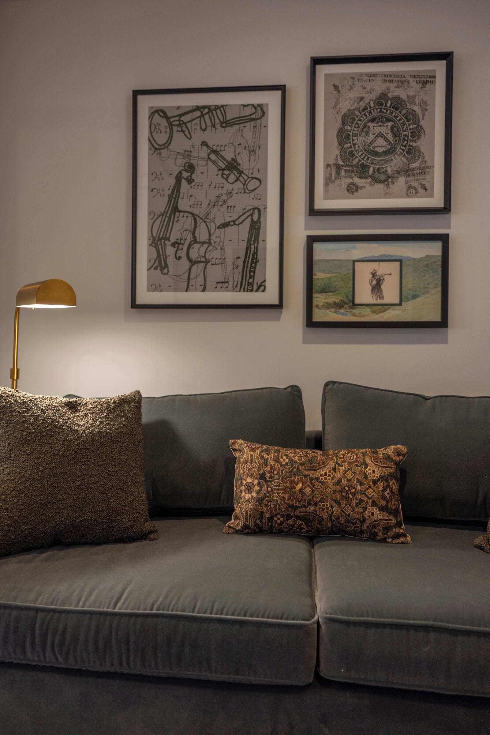 A grey sofa with patterned cushions, a framed abstract artwork, and a framed landscape painting on the wall.
