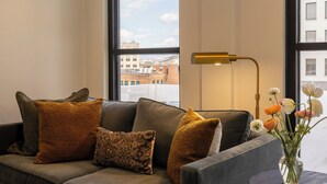 A modern living room with a grey sofa, a round coffee table, a floor lamp, and a vase with flowers. - The Promissory Hotel (Roanoke)