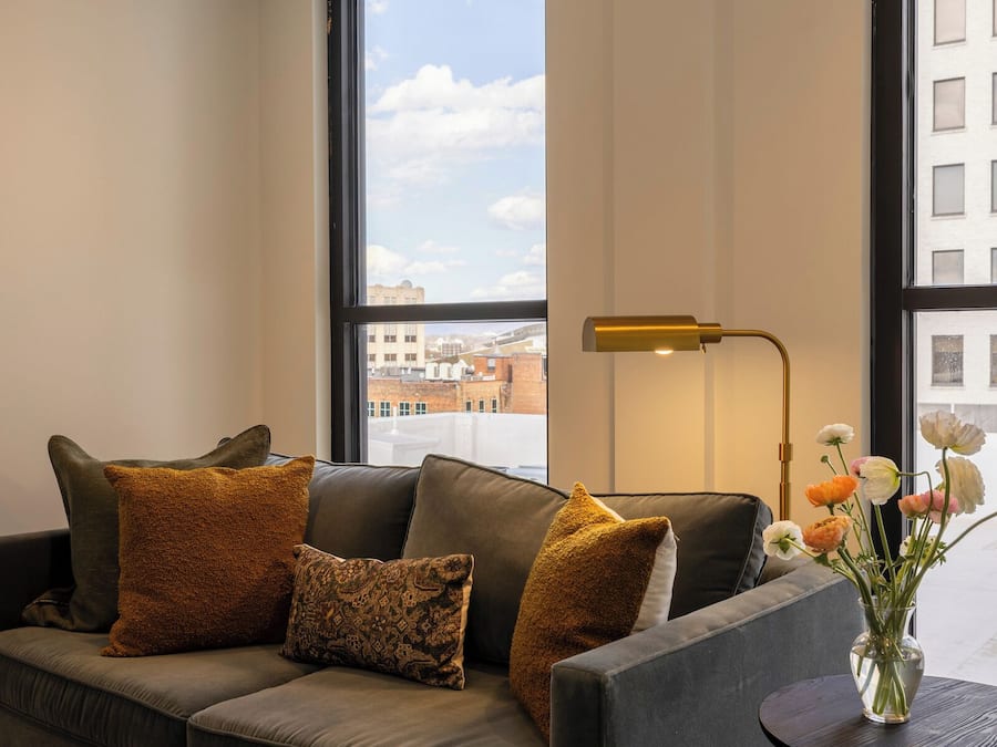 A modern living room with a grey sofa, a round coffee table, a floor lamp, and a vase with flowers.
