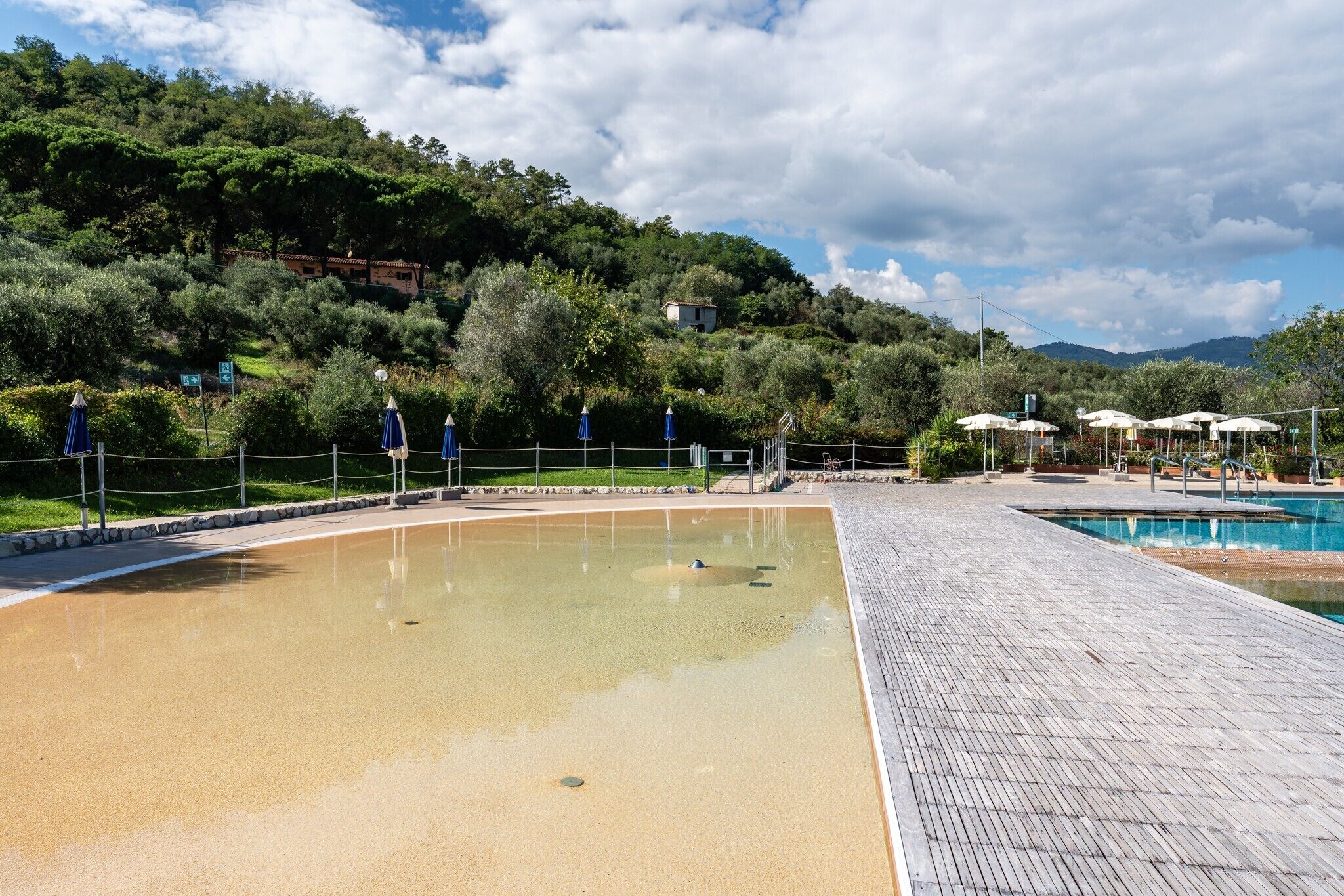 Ein Poolbereich mit Holzterrasse, umgeben von Grünflächen und Hügeln.