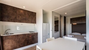 Une cuisine moderne équipée d’un évier, d’une cuisinière et d’un réfrigérateur, un coin repas avec une table et des chaises, et une chambre à coucher avec un lit et une table de chevet.