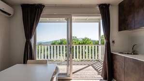 Une pièce dotée d’une porte-fenêtre coulissante donnant sur un balcon, d’une table blanche et d’un coin cuisine avec un évier.