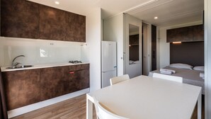 Une cuisine compacte équipée d’un évier, d’une cuisinière et d’un réfrigérateur, ainsi qu’une table à manger et un lit avec une tête de lit.