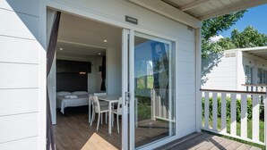 Une pièce comprenant un lit, une table et des chaises, une porte-fenêtre coulissante et une terrasse en bois.