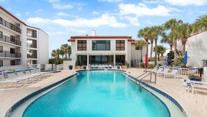 A swimming pool with lounge chairs and a building with balconies. - Las Brisas 502 (New Smyrna Beach)