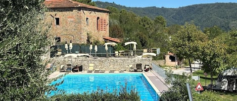 Un edificio de piedra con piscina, rodeado de vegetación y colinas.