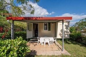A small, single-story building with a covered patio area, a table with chairs, and a door leading to an interior space. - Mobile Home 'Camping Belsito Olib 502' with Shared Pool, Wi-Fi and Air Conditioning (Vico)