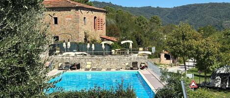 Un edificio de piedra con piscina, rodeado de vegetación y colinas.