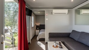A compact room with a bed, a sofa, a small table with a kettle, and an air conditioning unit.