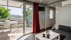A modern room with a sliding glass door to a balcony, a sofa, a table with a coffee maker, and a TV mounted on the wall.