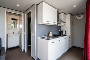 A compact kitchen with white cabinets, a stove, and a coffee maker.