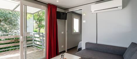 Una habitación moderna con un sofá gris, una mesita con taza y platillo, una cortina roja y un ventanal corredizo que da a un espacio exterior.