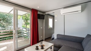 Un salon moderne avec un canapé gris, une table basse sur laquelle se trouvent une tasse et une soucoupe, un rideau rouge et une porte-fenêtre coulissante donnant sur un espace extérieur.