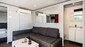 Une chambre moderne avec un canapé gris, une table blanche avec une machine à café, un miroir et un meuble blanc avec un évier.