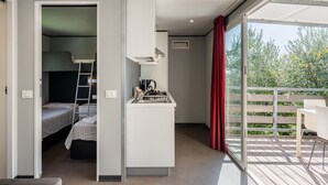 Une chambre compacte avec un lit superposé, une kitchenette et un balcon donnant sur un espace verdoyant.