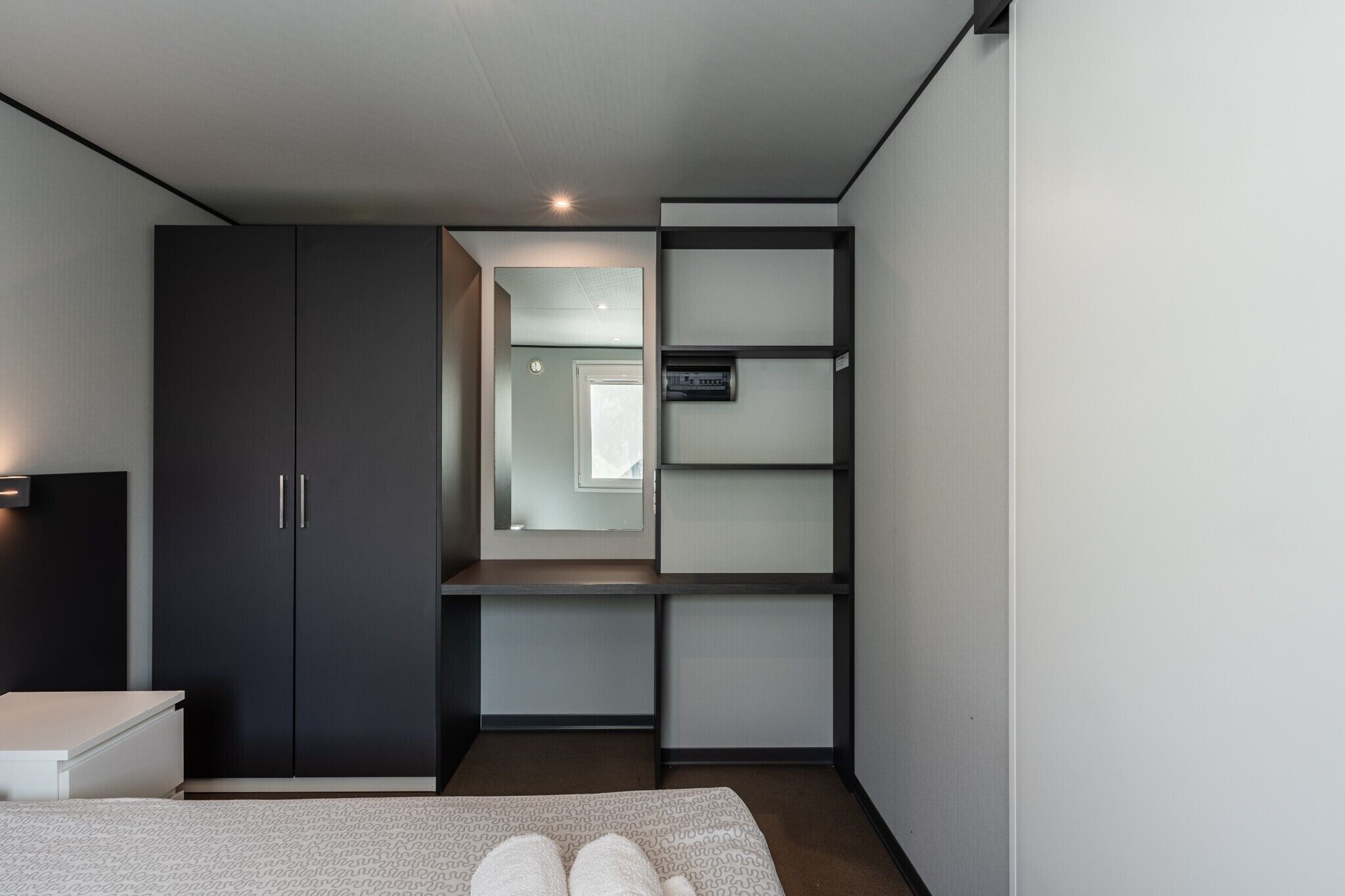 Een slaapkamer met een bed, een garderobe, een bureau en een plank.
