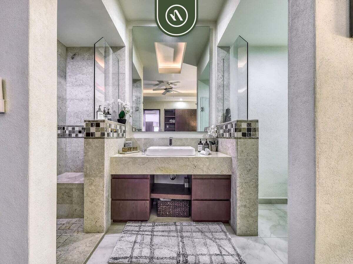 A modern bathroom with a large mirror, a central sink, and a ceiling fan.