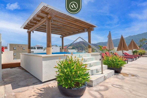 A rooftop pool area with a wooden pergola, lounge chairs, and potted plants.