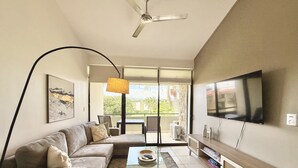 A modern living room with a sofa, coffee table, and TV. There's a balcony with a view of greenery. - Brand New lake view Penthouse with A/C, pool, gym, tennis in common area (Río Oro)