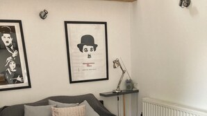 Ett sovrum med en säng, kuddar, ett sängbord med en lampa och inramade konstverk på väggen.