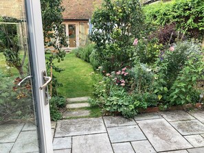 A garden pathway leading to a house with a brick roof, surrounded by various plants and flowers. - Remarkable 1-bed Cottage in Orwell Cambridgeshire (Royston)