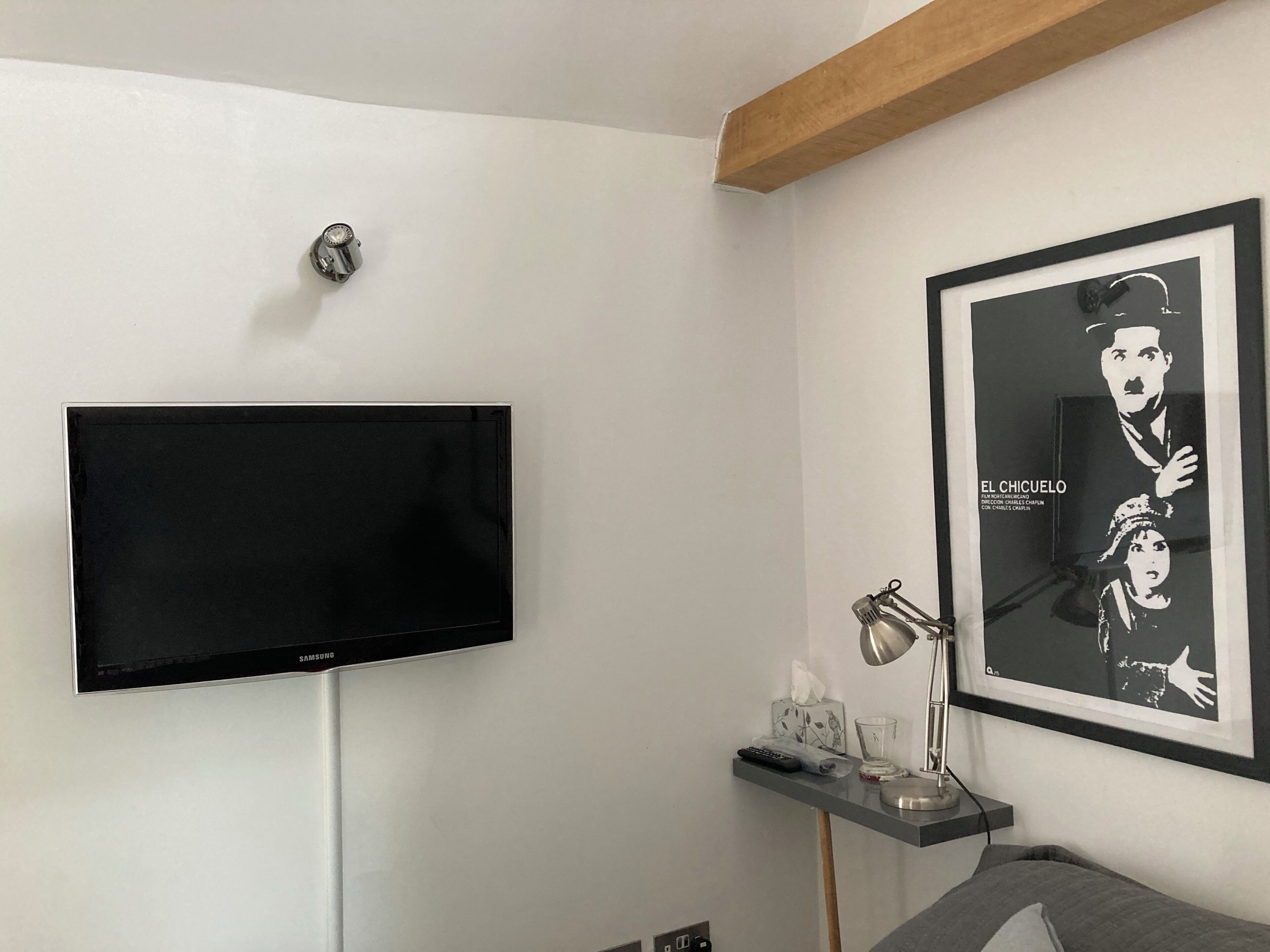 Une chambre moderne équipée d’un téléviseur fixé au mur, d’une affiche encadrée, d’une table de chevet avec une lampe et d’un lit.