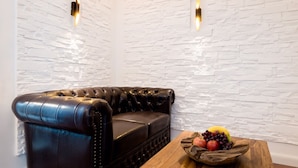 A black leather sofa against a white brick wall with two wall-mounted lights. A wooden table with a fruit bowl is in front of the sofa. - High-quality, centrally located apartment in the middle of the city (Rudolstadt)