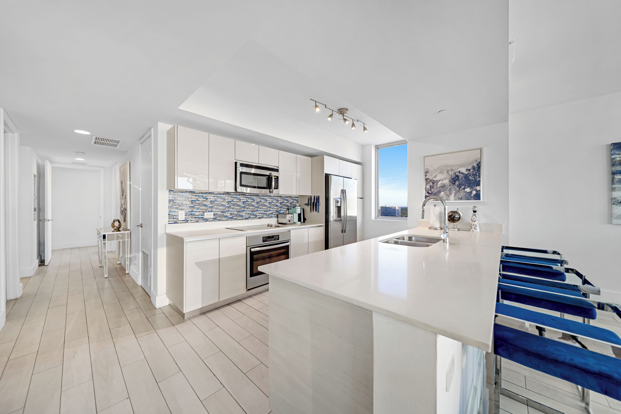 A modern kitchen with white cabinetry, a large island, and a blue bar stool.