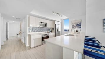A modern kitchen with white cabinetry, a large island, and a blue bar stool.