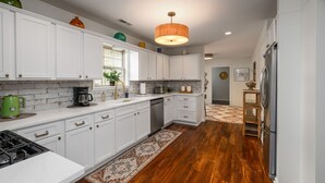 Une cuisine moderne avec des meubles blancs, un réfrigérateur en acier inoxydable et un plancher en bois.