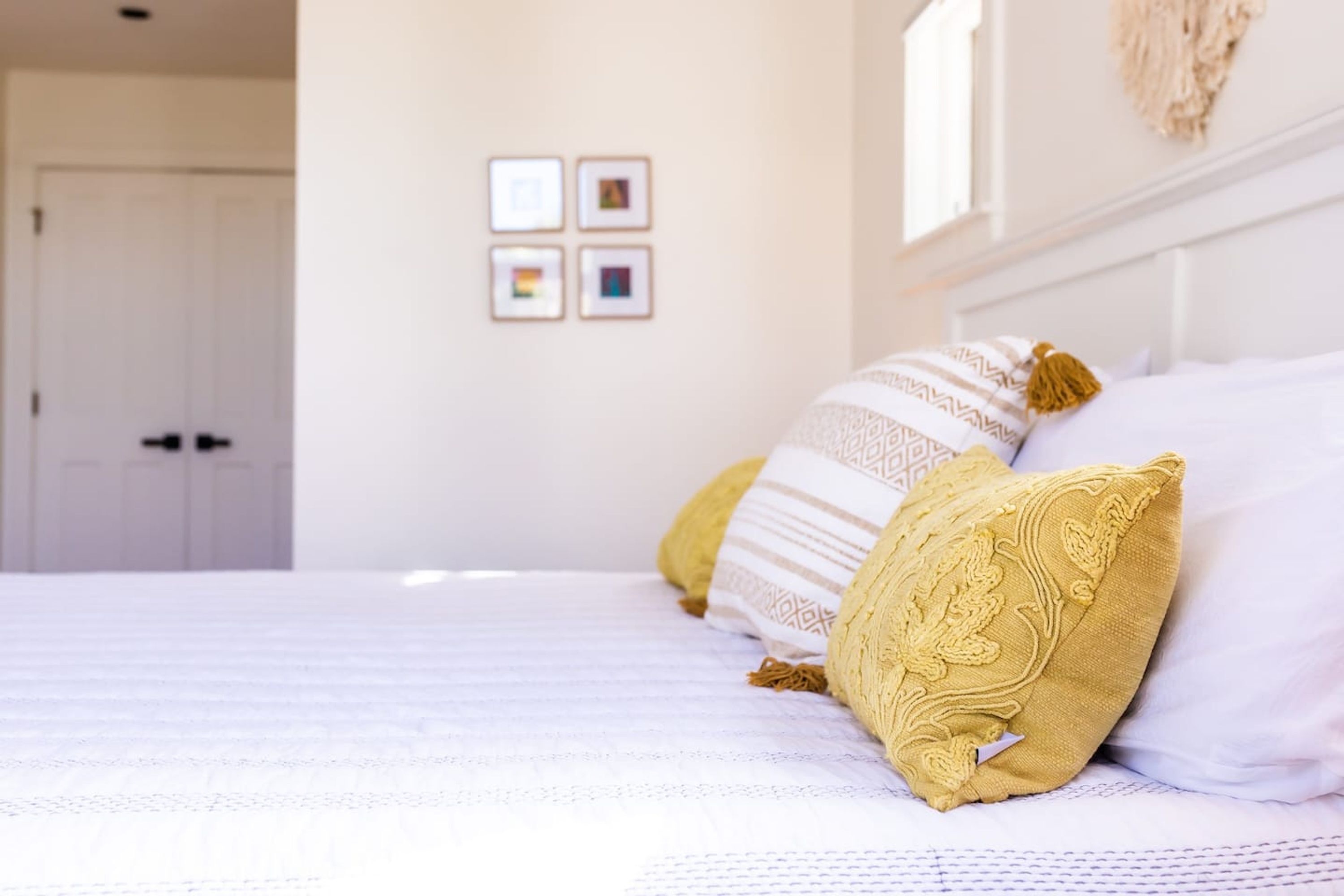 A neatly made bed with patterned pillows and a plain wall with framed pictures.