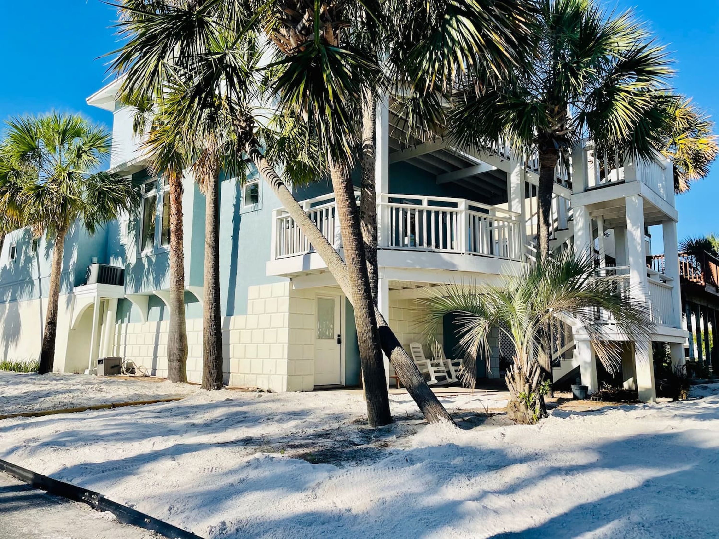 A beachfront property with a two-story building, a balcony, and palm trees.