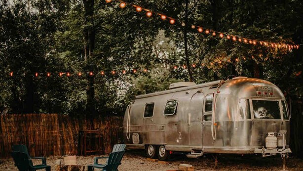A vintage trailer with a small table and two chairs in a wooded area. - Boho Blue & Airstream Nearby all Things Memphis (Memphis)