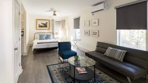 A modern, well-lit room with a bed, a blue armchair, a dark sofa, and a glass coffee table. - Boho Blue & Airstream Nearby all Things Memphis (Memphis)