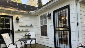 A corner of a house with a black door, white siding, a small table with two chairs, and string lights above. - Moody Blues Studio Perfect for Work or Romance (Memphis)