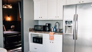 A modern kitchen with white cabinets, a stainless steel refrigerator, a built-in microwave, and a coffee maker. - Moody Blues Studio Perfect for Work or Romance (Memphis)
