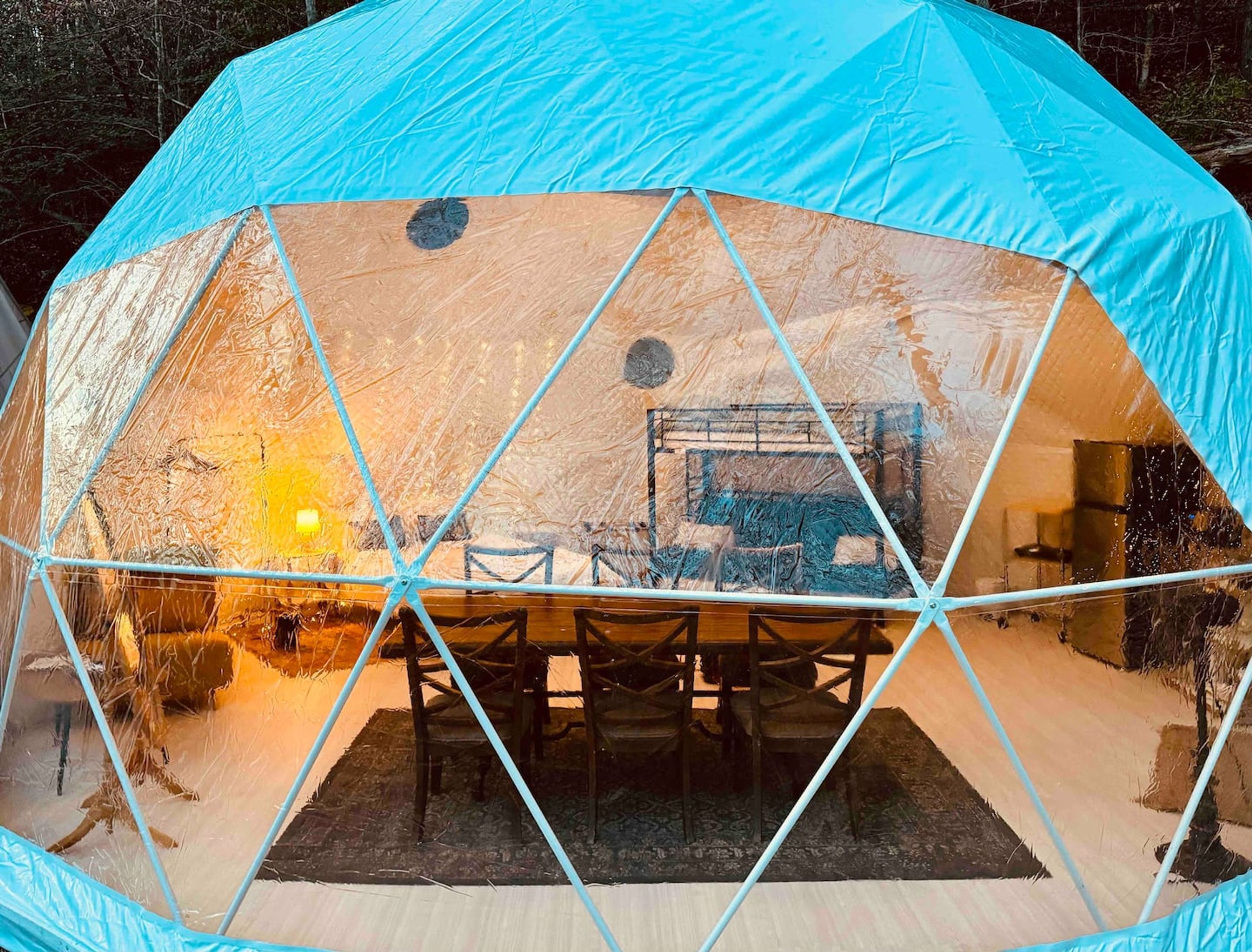 A geodesic dome structure with a central table and chairs, surrounded by a patterned rug.