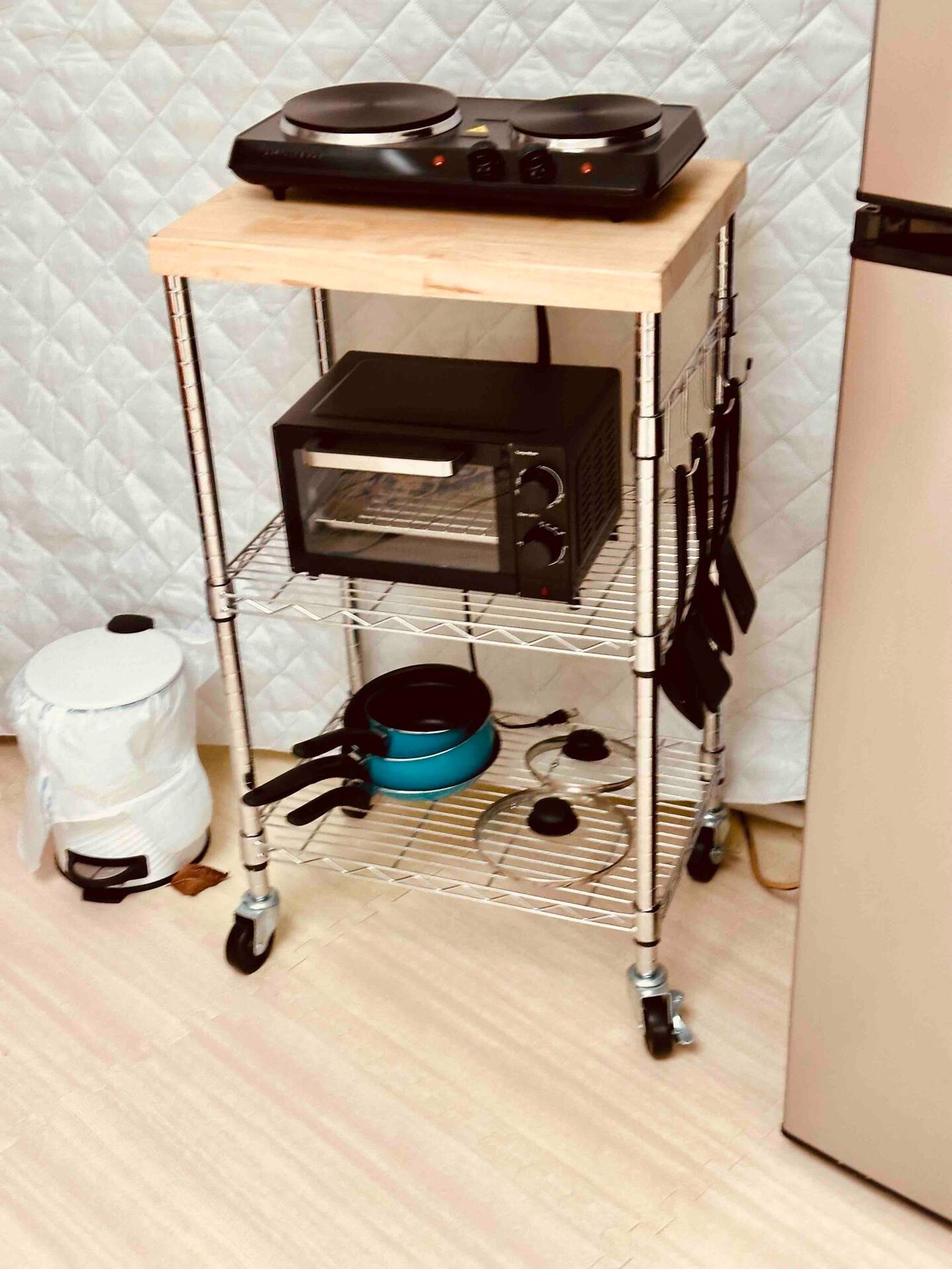 Un chariot de cuisine avec une machine à café, un grille-pain et une casserole, le tout posé sur un sol carrelé.