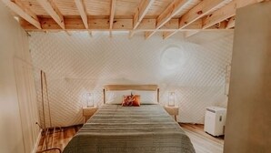 A small, cozy bedroom with a wooden ceiling, a single bed with a green blanket, two bedside tables with lamps, and a small air conditioning unit. - Slate Crossing Creekside Dome (Cosby)
