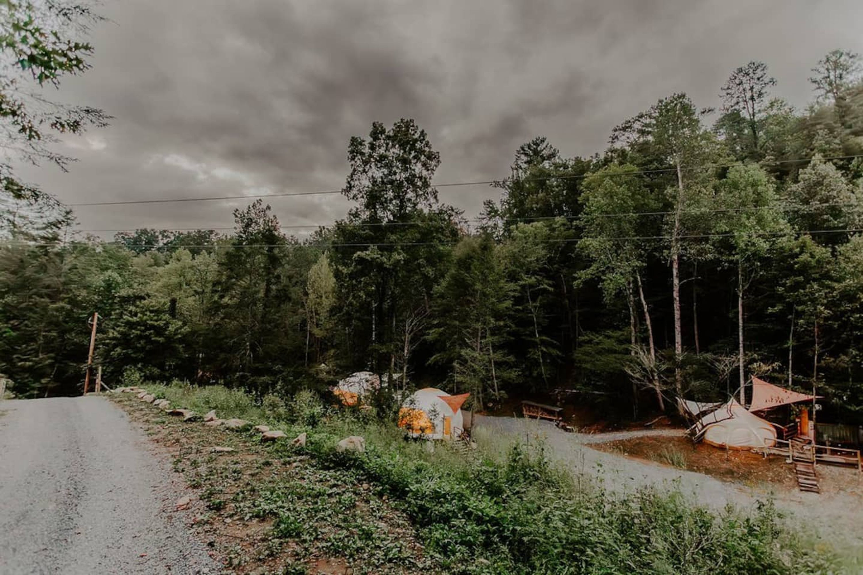 A rural road with a campsite featuring tents and a small wooden structure.