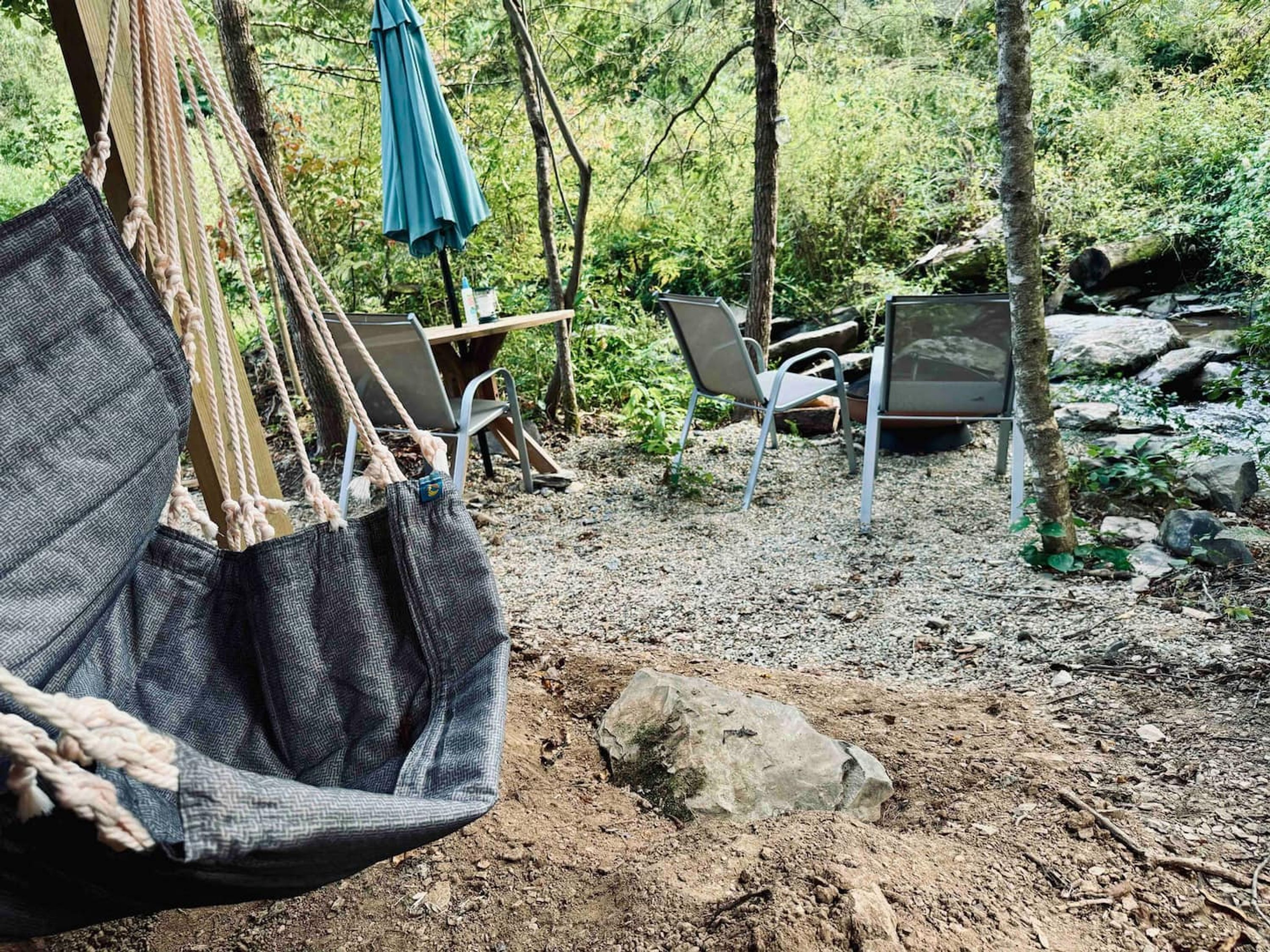 Eine Hängematte, zwei Stühle und ein Tisch inmitten von Wald, Felsen und Grünpflanzen.