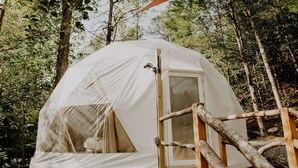 A dome-shaped tent with a wooden deck and a glass door, set in a forested area. - Whispering Waters Dome Getaway (Cosby)