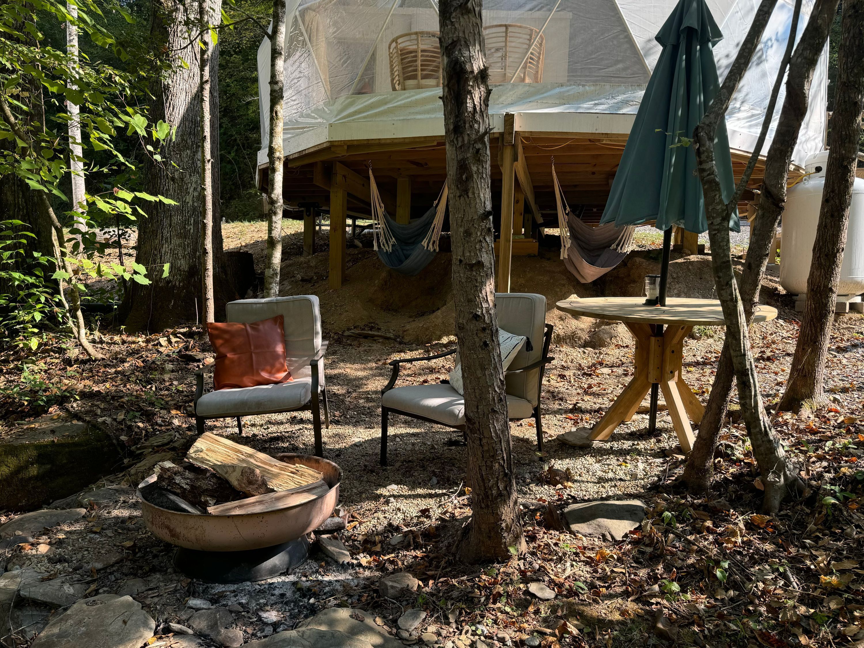 A rustic outdoor seating area with a hammock, a table, and chairs.